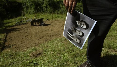 Antonio Piedrafita sostiene la foto de sus padres con él de niño al lado de la fosa común donde están sus restos en Valdediós (Asturias). / ELOY ALONSO / ARMH 