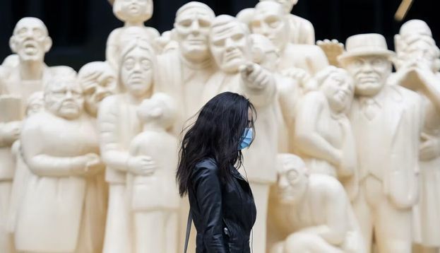 A woman wears a face mask as she walks by the sculpture ‘The Illuminated Crowd’ on a street in Montréal. Vulnerable people may benefit from measures like face masks even after the COVID-19 pandemic. THE CANADIAN PRESS/Graham Hughes