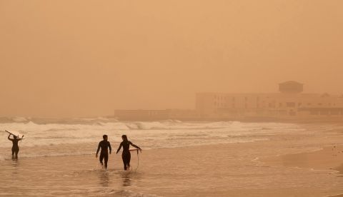 Varios surfistas se adentran en el mar de Playa Blanca, cubierta por una densa calima procedente de África, este domingo en Puerto del Rosario (Fuerteventura).. EFE/Carlos de Saá