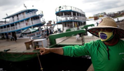 Un hombre con tapabocas de diseño de la bandera brasileña señala hacia el río Amazonas en Manaos (Brasil).